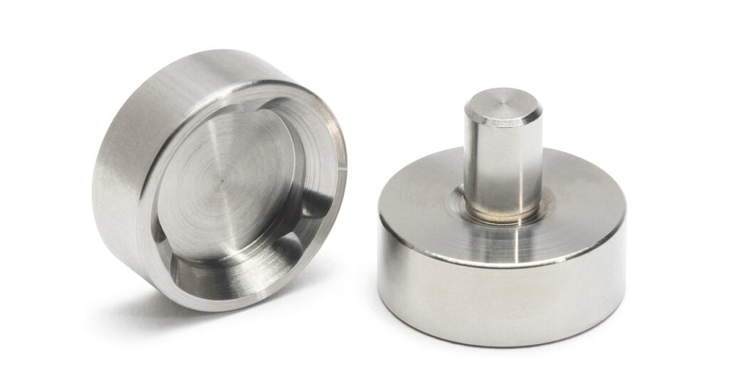 Two brushed metal cylindrical adapters. One is upright with a center pin, and the other shows a recessed circular face.